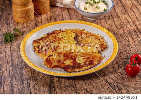 Crispy golden potato pancakes draniki served on white plate with yellow rim, sour cream, cherry tomatoes, and parsley on rustic wooden table Crispy golden potato pancakes draniki served on white plate with yellow rim, sour cream, cherry tomatoes, and parsley on rustic wooden table 142449951