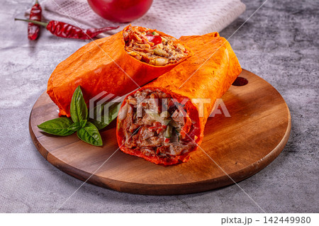 Chicken shawarma wrap sliced open on wooden board with basil and red chili peppers Chicken shawarma wrap sliced open on wooden board with basil and red chili peppers 142449980