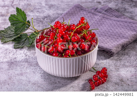Fresh red currants in white ceramic bowl with green leaves on textured gray surface 142449981