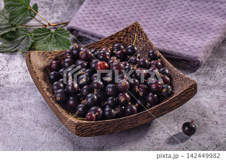 Fresh black currants in wooden bowl with green leaves and purple cloth Fresh black currants in wooden bowl with green leaves and purple cloth 142449982