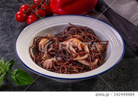 Black spaghetti with squid and mussels in white bowl on dark surface with cherry tomatoes and basil 142449984
