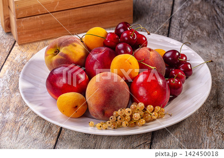 Assorted fresh summer fruits on white plate with rustic wood background 142450018