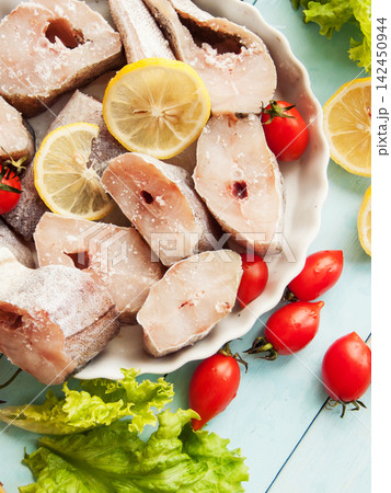 Fresh pollock seafood steaks with lettuce and cherry tomatoes seasoned with salt and lemon in pan 142450944