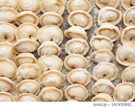 Raw homemade handmade russian pelmeni dumplings rows sprinkled with flour on metal tray 142450982