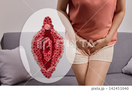 Woman sitting on a sofa holding her pelvic area next to a floral vulva illustration. Female intimate flora balance and reproductive wellness concept 142451040