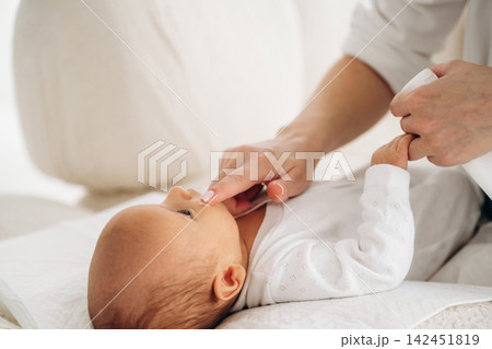 Infant lying on a soft surface while an adult hand gently touches the baby's face, creating a tender moment in a bright and cozy indoor setting 142451819