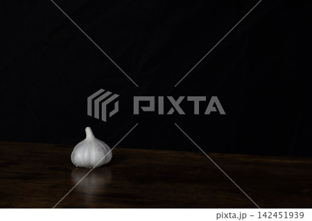 Garlic bulb on a dark wooden surface with a black background 142451939