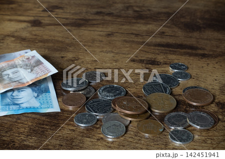 British pound sterling currency, including banknotes and various coins, scattered on a wooden surface 142451941