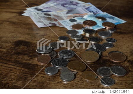 British Pound Sterling banknotes and coins scattered on a wooden table British Pound Sterling banknotes and coins scattered on a wooden table 142451944