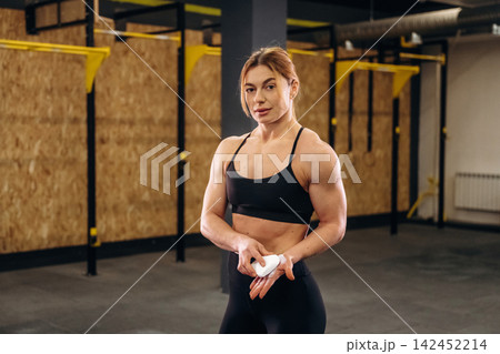 Female athlete applying chalk to hands in a gym setting, showcasing strength and preparation for weightlifting with equipment visible in the background 142452214