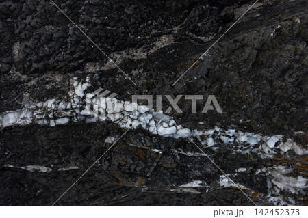 Dark igneous rock texture showing a prominent white quartz vein, creating a natural abstract pattern 142452373