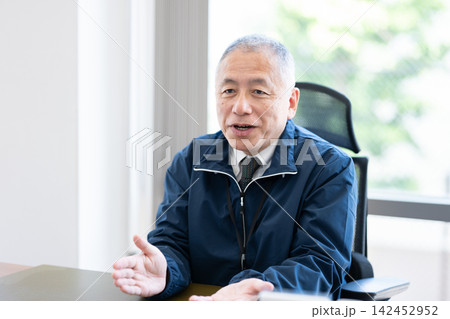 オフィスでデスク越しに身振り手振りを交えて話すシニア男性役員 オフィスでデスク越しに身振り手振りを交えて話すシニア男性役員 142452952