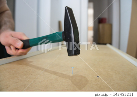 Raised hammer above a nail waiting in a hardboard back panel 142453211