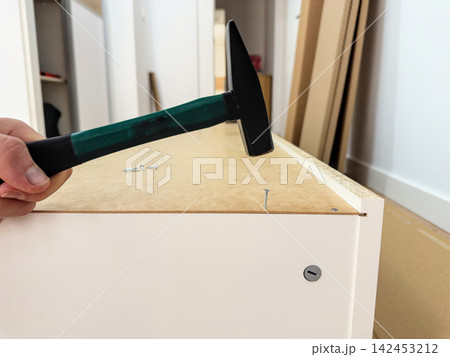 Hammer over a nail in the hardboard back of a tall cabinet 142453212