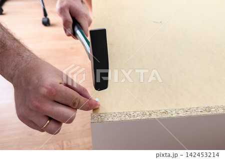 Man holds a nail and swings a hammer at a hardboard back panel 142453214