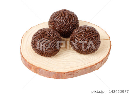 Three traditional Brazilian chocolate brigadeiros coated in sprinkles, on a round wooden base, isolated against a white background. Three traditional Brazilian chocolate brigadeiros coated in sprinkles, on a round wooden base, isolated against a white background. 142453977