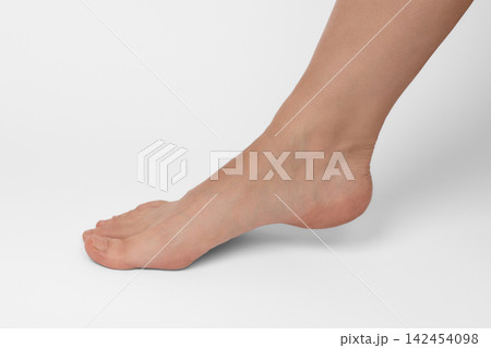 Female foot standing on tiptoe against a plain white background. Elegant foot posture, arch flexibility, and podiatry concept Female foot standing on tiptoe against a plain white background. Elegant foot posture, arch flexibility, and podiatry concept 142454098