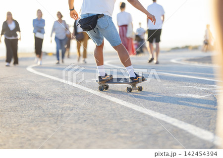 Skateboarding on a path as people walk by during the day at a busy outdoor area Skateboarding on a path as people walk by during the day at a busy outdoor area 142454394
