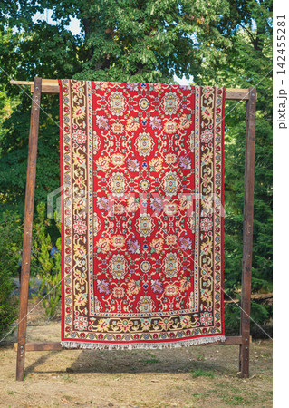 Traditional red Kotel carpet with ornamental floral and geometric pattern displayed outdoors in park Bulgaria. Bright Bulgarian textile heritage and handcrafted rug artistry Traditional red Kotel carpet with ornamental floral and geometric pattern displayed outdoors in park Bulgaria. Bright Bulgarian textile heritage and handcrafted rug artistry 142455281