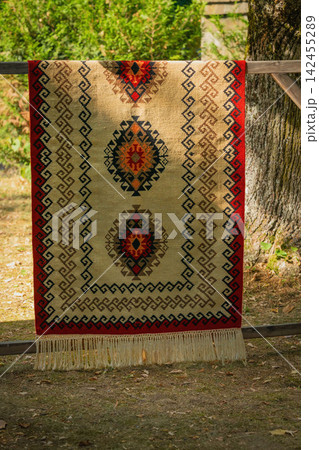 Traditional Kotel carpet with geometric ethnic ornament and decorative fringe displayed outdoors in Bulgaria. Authentic Bulgarian textile craftsmanship and folk heritage Traditional Kotel carpet with geometric ethnic ornament and decorative fringe displayed outdoors in Bulgaria. Authentic Bulgarian textile craftsmanship and folk heritage 142455289