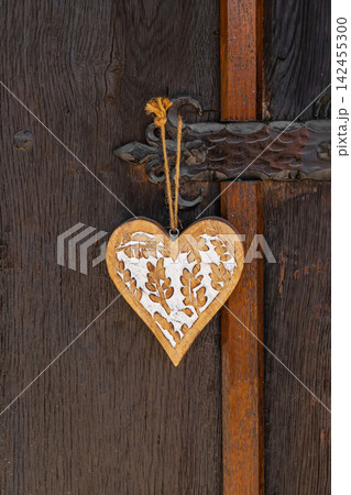 Wooden heart ornament on rustic wooden door. Handmade wooden heart ornament with carved floral decoration on old rustic wooden door. Natural folk decor, romantic symbol, warm home decor 142455300