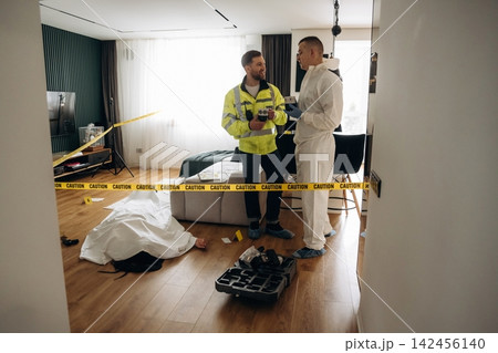 Forensic expert and police detective discussing evidence at a murder scene with caution tape, body covered in white sheet, and tools on the floor in a modern interior Forensic expert and police detective discussing evidence at a murder scene with caution tape, body covered in white sheet, and tools on the floor in a modern interior 142456140