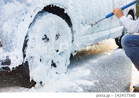 A person sprays foam onto a car wheel and side during a detailed cleaning process 142457560