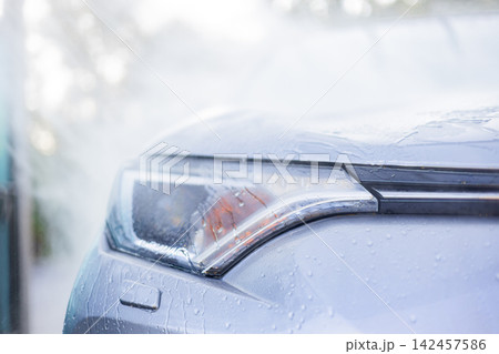 Close-up of a car's headlight being washed with water droplets on the surface, creating a clean and shiny appearance Close-up of a car's headlight being washed with water droplets on the surface, creating a clean and shiny appearance 142457586