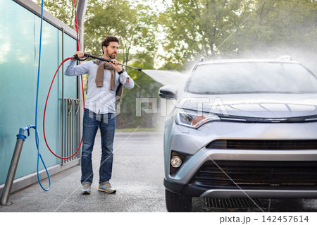 A caucasian man is actively cleaning his silver SUV at a self-service car wash station using a high-pressure water spray A caucasian man is actively cleaning his silver SUV at a self-service car wash station using a high-pressure water spray 142457614