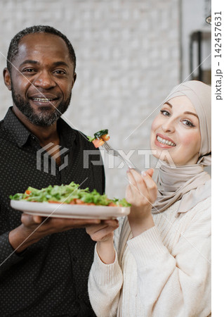 A smiling African man and a woman in a hijab share a healthy salad, highlighting togetherness and good food A smiling African man and a woman in a hijab share a healthy salad, highlighting togetherness and good food 142457631