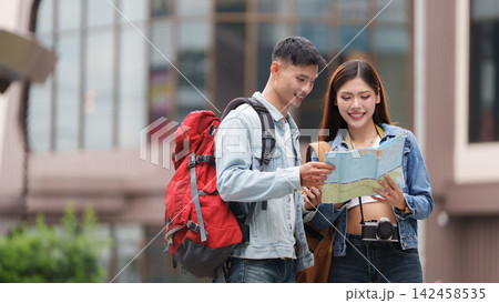 Asian couple looking at paper map while travelling outdoors in city for tourism Asian couple looking at paper map while travelling outdoors in city for tourism 142458535