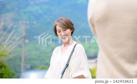 笑顔で語り合う熟年夫婦、背景は緑豊かな山々 笑顔で語り合う熟年夫婦、背景は緑豊かな山々 142458621
