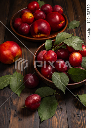 Ripe plums and nectarines in bowls on rustic wooden table 142458789