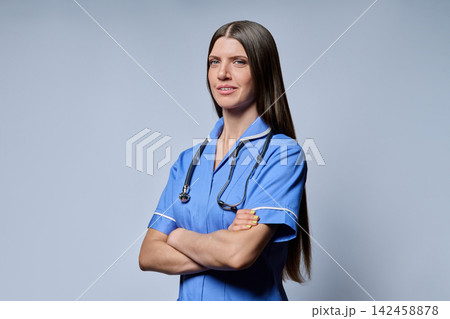 Three-quarter portrait of confident female nurse standing with folded arms on grey background 142458878
