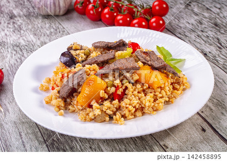 Bulgur pilaf with beef and roasted vegetables on white plate 142458895