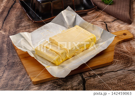 Fresh butter block with slices on parchment paper over wooden cutting board Fresh butter block with slices on parchment paper over wooden cutting board 142459063
