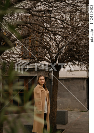 Girl with dreadlocks stands by bare trees in urban area on a cloudy day Girl with dreadlocks stands by bare trees in urban area on a cloudy day 142459402