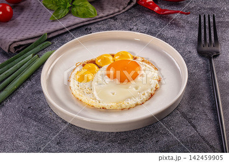 Fried egg with multiple yolks on white plate with green onions and basil 142459905