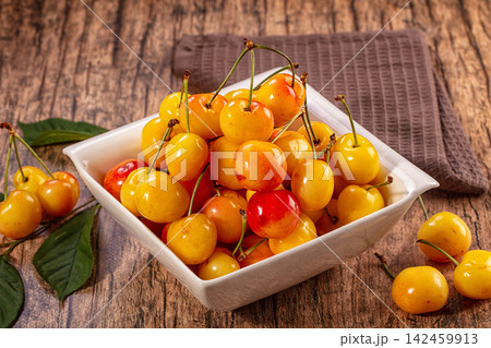 Yellow cherries in white bowl on rustic wooden table with green leaves Yellow cherries in white bowl on rustic wooden table with green leaves 142459913