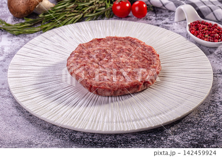 Raw beef patty on textured white plate with rosemary cherry tomatoes and peppercorns Raw beef patty on textured white plate with rosemary cherry tomatoes and peppercorns 142459924