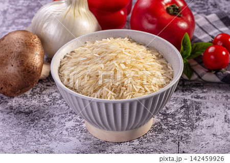 Bowl of uncooked rice with fresh vegetables on rustic surface 142459926