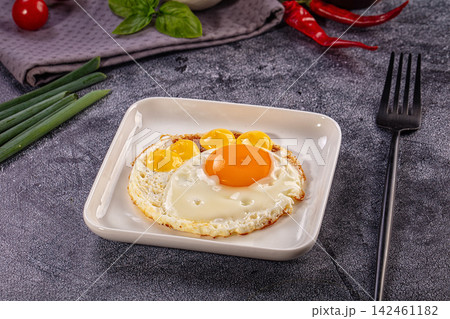 Fried egg with multiple yolks on white plate with green onions and red chili peppers Fried egg with multiple yolks on white plate with green onions and red chili peppers 142461182