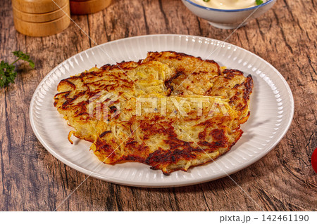 Crispy golden potato pancakes on white plate with rustic wooden background 142461190