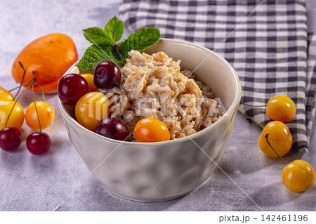 Oatmeal bowl with fresh cherries and mint on textured surface Oatmeal bowl with fresh cherries and mint on textured surface 142461196