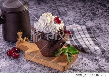 Chocolate cupcake with whipped cream and cherry on wooden board 142461205