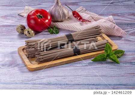 Soba noodles on wooden board with tomato garlic chili and basil on rustic table 142461209