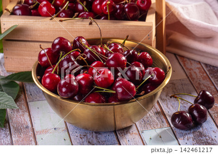 Fresh red cherries in brass bowl on rustic wooden table 142461217