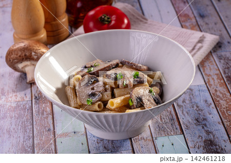 Rigatoni pasta with mushrooms and green onions in white bowl on rustic wooden table Rigatoni pasta with mushrooms and green onions in white bowl on rustic wooden table 142461218