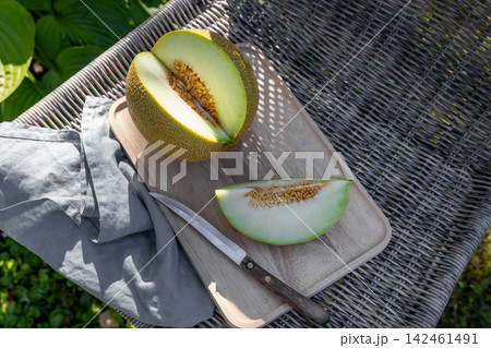Cut Melon on Wooden Tray on Wicker Chair in Sunny Summer Garden Cut Melon on Wooden Tray on Wicker Chair in Sunny Summer Garden 142461491