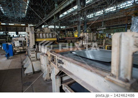 Industrial factory interior with heavy machinery processing metal sheets under high ceiling with steel beams and natural light Industrial factory interior with heavy machinery processing metal sheets under high ceiling with steel beams and natural light 142462486